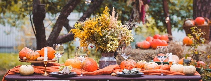 fall themed holiday table setting arrangement for a seasonal party, glasses, pumpkins, candles, field flowers