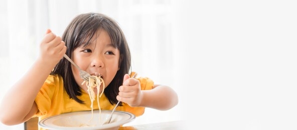 hungry face and enjoy eating concept.little asian girl enjoy eating with spaghetti carbonara with cheese on a plate in lunch time at restaurant.kid eating pasta.delivery food, delicious face.