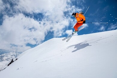 man skier athlete makes a jump in flight on a snowy slope against the backdrop of a blue sky of mountains and clouds. freeride and extreme skiing for men