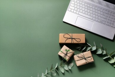 online holiday shopping concept. lap top, gift boxes and eucalyptus twigs on deep green background.
