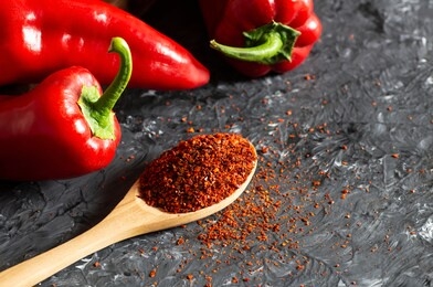 fresh capia peppers and chili flakes or powder in wooden spoon on grey rustic table, healthy turkish spice