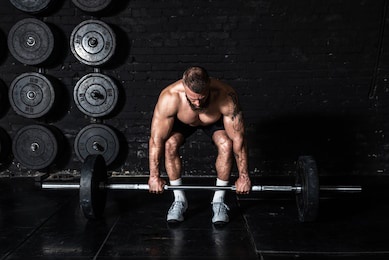 young strong muscular fit man holding heavy barbell weight and starting weightlifing workout in the gym