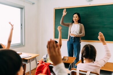 asian school teacher with students raising hands. young woman working in school with arm raised, school children putting their hands up to answer question, enthusiasm, eager, enjoyment.