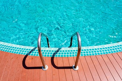 steel ladder on wooden plank floor into empty clear turquoise swimming pool.
