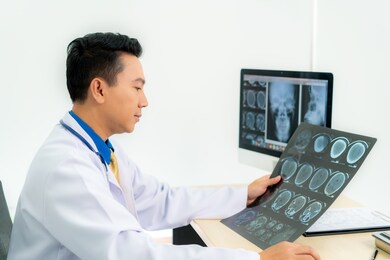 asian man doctor holding and looking to examining x-ray of the patient skull and brain in a medical clinic at hospital. 