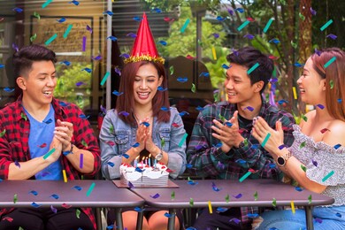 group of happy people clapping hands and singing together while celebrating a birthday party for their friend while sitting in the cafe