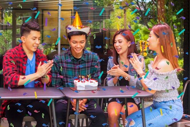 smiling people clapping hands and singing together while celebrating a birthday party for their friend while sitting in the cafe