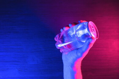 a transparent soda can in the neon lights on the black table background.