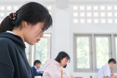 asian high school or university student reading question exam test class and using pencil writing on paper answer sheet, doing final exam attending in examination classroom with students in uniform