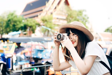 young adult asian woman wearing hat and backpack local travel. take a photo with camera. sightseeing on summer holidays in bangkok, thailand.