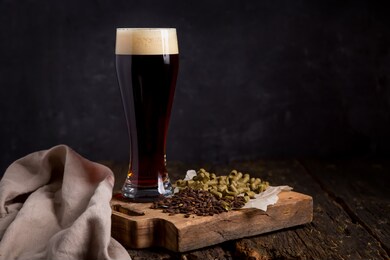 homemade dark beer with beautiful foam in a glass glass on a dark wooden table chocolate malt, granulated hops. copy space