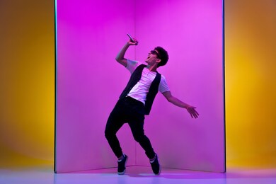 young male musician, singer performing on pink-orange background in neon light. concept of music, hobby, festival, entertainment, emotions. joyful party host, singer, portrait of artist.