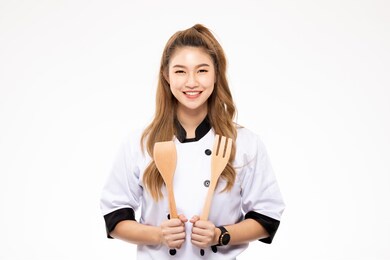 beautiful asian chef woman smile and holding wooden spatula and fork isolated on white background,happiness and cheerful professional chef concept
