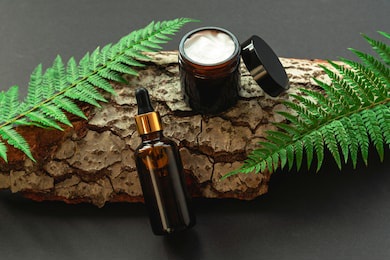 cosmetic bottle and cream jar on black background with wood and greenery. natural cosmetics concept. top view.