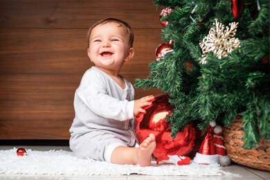 cute child with christmas tree.  happy baby sitting near a fir tree and holding a christmas ornament and smiling