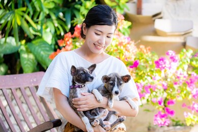 a japanese woman holding two cute puppies in a colorful garden