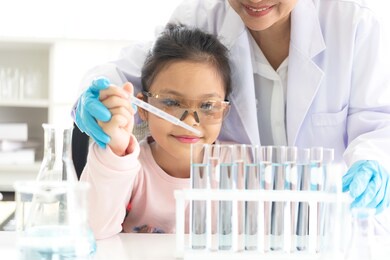 asian children analyzing study evaluating microscope with scientist. health care researchers doing some research with dropper chemical testing and working in life science laboratory