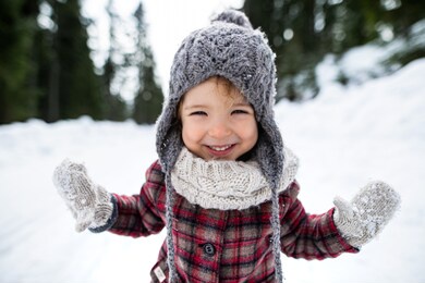front view portrait of cheerful small girl standing in winter nature, looking at camera.