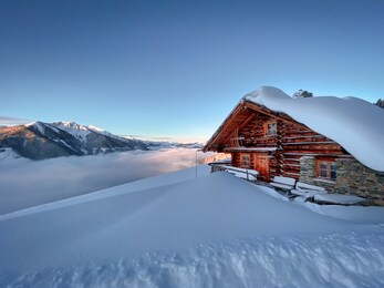 snow covered mountain hut old farmhouse in the ski region of saalbach hinterglemm in the austrian alps at sunrise against blue sky