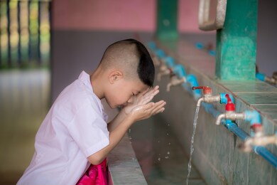 side view. male student washing his face at washbasin in the school. child cleanse their bodies. asian boy wearing a school uniform is 5 years old.