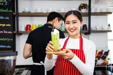 beautiful barista holding out a glass of iced tea. matcha green tea drink in a glass with milk cream. useful latte. vintage tone and soft focus
