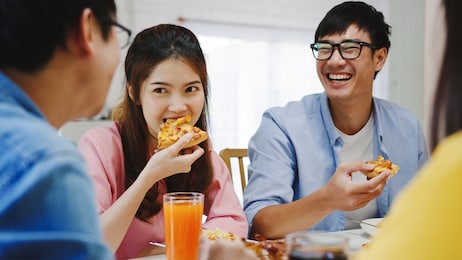 happy young friends group having lunch at home. asia family party eating pizza food and laughing enjoying meal while sitting at dining table together at house. celebration holiday and togetherness.