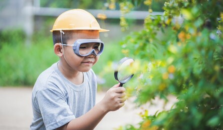 asian kid looking at leaves and holding magnifying glass for explore.