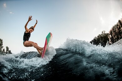 young athletic woman in wetsuit try to balance on surf style wakeboard on splashed river wave