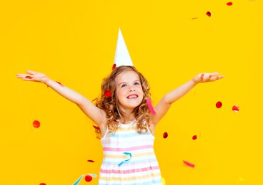 portrait of a little beautiful girl celebrating her birthday. the kid is throwing colorful confetti. yellow studio background. the child is having fun