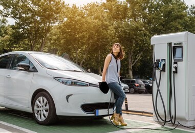 young beautiful woman is charging her electric car at the charging station situated in city. eco friendly transport concept