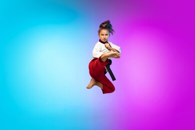 practice. karate, taekwondo girl with black belt isolated on gradient background in neon light. little caucasian model, sport kid training in motion and action. sport, movement, childhood concept.