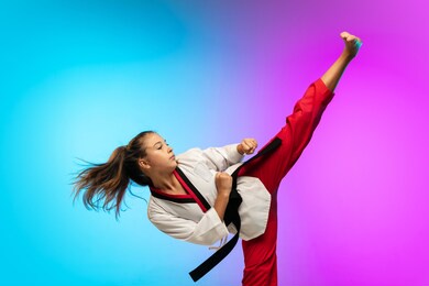 practice. karate, taekwondo girl with black belt isolated on gradient background in neon light. little caucasian model, sport kid training in motion and action. sport, movement, childhood concept.
