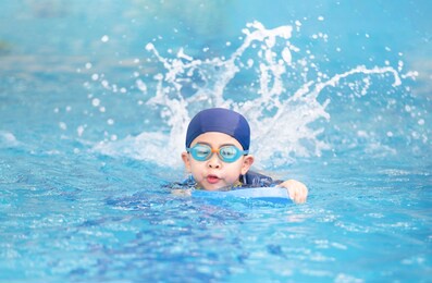 asia cute boy wearing swimming suit and goggles used foam to practice swimming in swimming pool. healthy kid enjoying active lifestyle. refreshing and relax to exercise on summer holiday