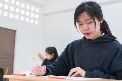 asian high school or university student reading question exam test class and using pencil writing on paper answer sheet, doing final exam attending in examination classroom with students in uniform