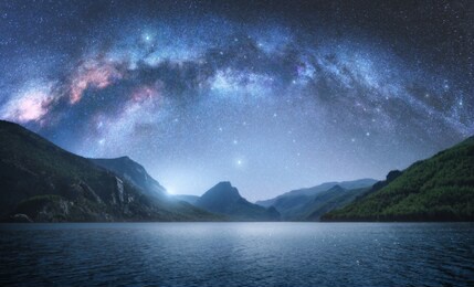 arched milky way over the beautiful mountains and blue sea at night in summer. colorful landscape with bright starry sky with milky way arch, moonlight, constellation, water. galaxy. nature and space