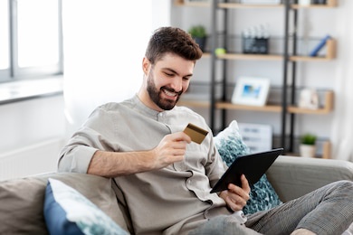 technology, people and online shopping concept - happy smiling man with tablet pc computer and credit card at home