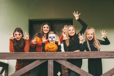 a group of children celebrating halloween on the street near the house in nature in costumes and make-up with a pumpkin lantern, plays and laughs