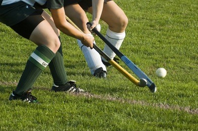 two girls battle for control of the ball in a field hockey game.
