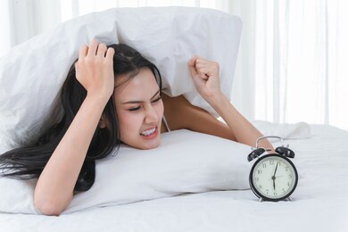 asian girl cute and beautiful feeling bored in waking up after the alarm clock rings on bed.