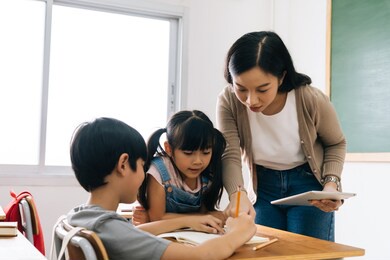 asian school teacher using digital device with children in classroom at school, technology, learning, development.