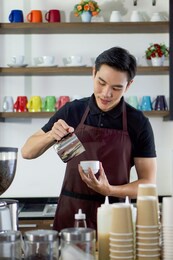 young asian man pouring milk into coffee making espresso. professional barista preparing coffee on counter.