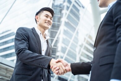 asian businessmen making handshake in the city with highrise building in background. partnership agreement is successful after complete the negotiation. business deal, merger and acquisition concepts.