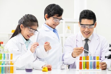 young asian boy and girl smile and having fun while learning science experiment in laboratory with teacher in classroom. study with scientific equipment and tubes. education concept.