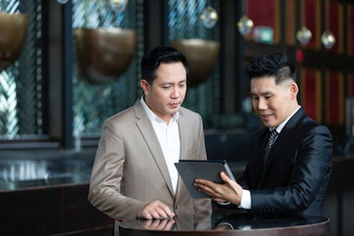 group of asian businessman wearing suits talking using digital tablet together while standing in conference room. two asian businessman discussing ideas concept. business, people  