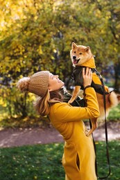 girl wearing a yellow coat walking in a autumn park with a cute fanny dog  shiba inu wearing a green coat