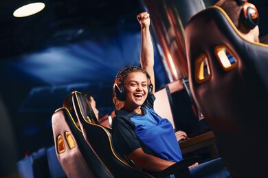 young happy mixed race girl, female cybersport gamer raising hand up and smiling at camera while participating in esport tournament