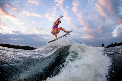 athletic man in bright clothes actively riding large wave doing jumps and tricks on the surf style wakeboard