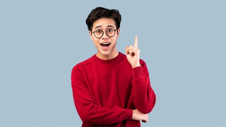 wow, eureka. portrait of emotional asian student having great idea, finding inspiration or solution to problem. excited amazed guy in glasses with open mouth pointing finger up over studio background