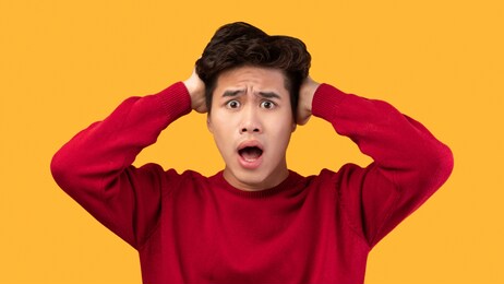 people, human emotions and feelings concept. portrait of shocked scared asian man with open mouth grabbing head looking at camera in amazement, isolated over yellow studio background