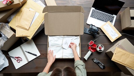 top above closeup view of female online store small business owner entrepreneur packing package post shipping box preparing delivery parcel on table. ecommerce dropshipping shipment service concept.